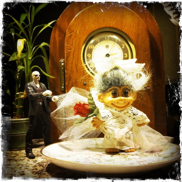 Grandma made a dress for the troll doll out of doily and ribbon.  She then arranged the doll with the figurine in front of the clock.